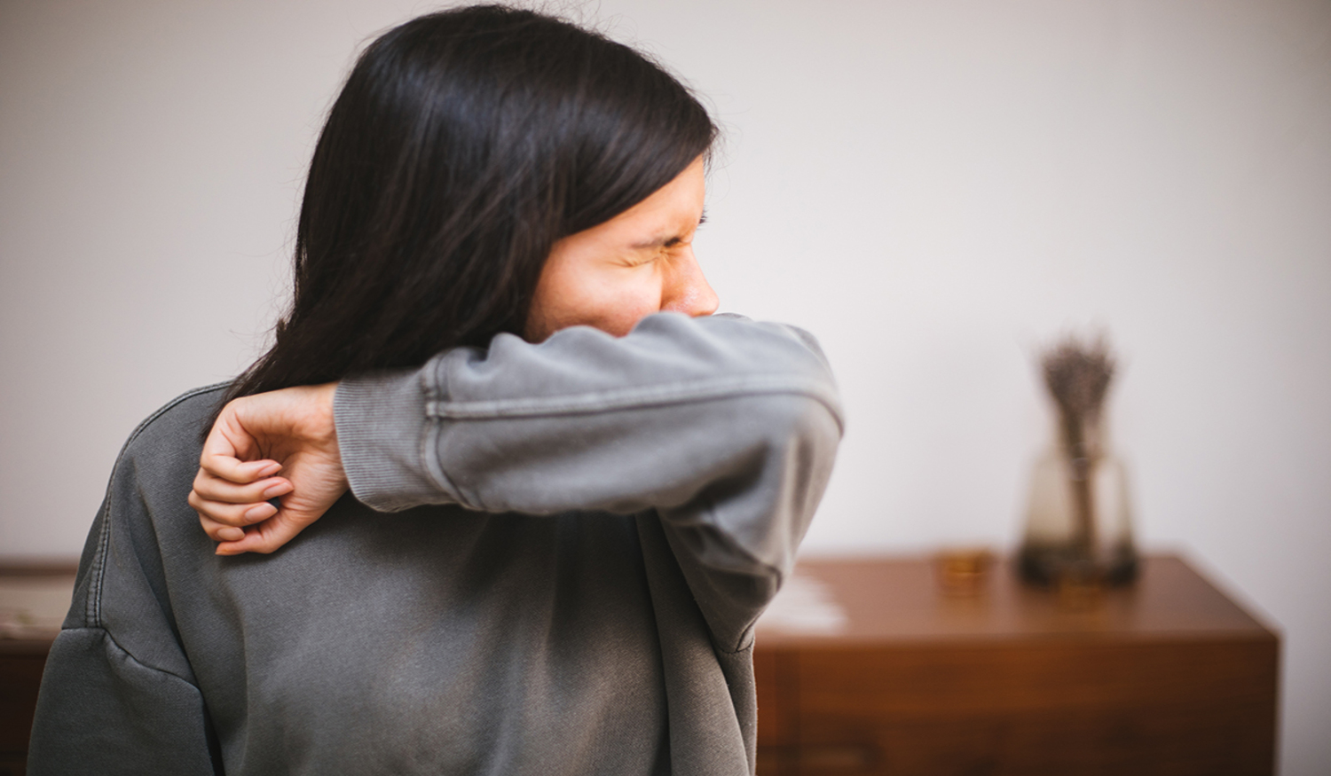 A woman sneezes into the crook of her arm