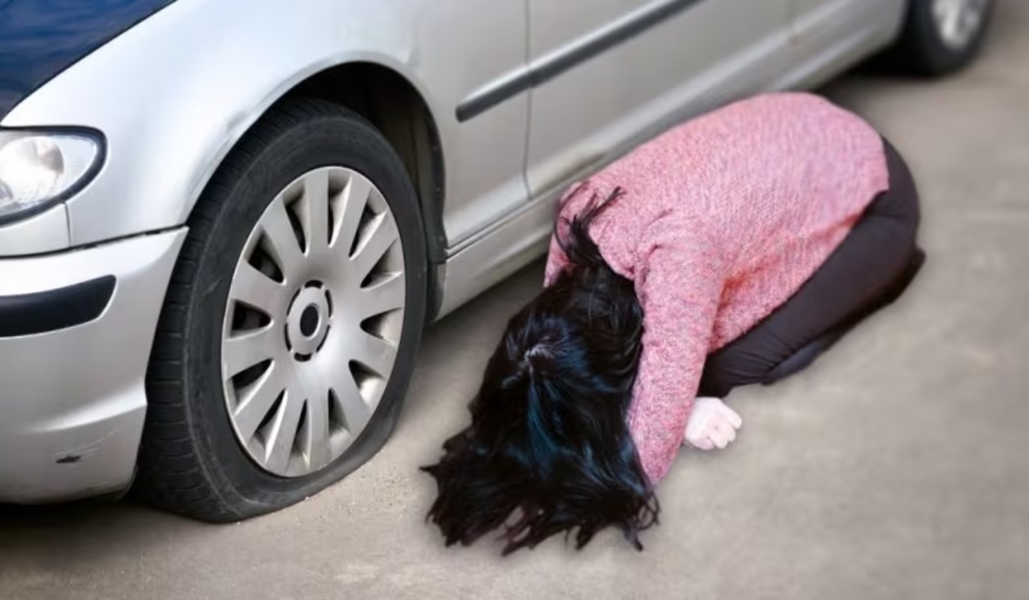 Deflated - a woman on her face near a car with a flat tire
